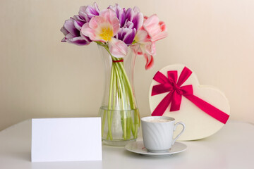 A bouquet of open pink and purple tulips, a gift box in the shape of a heart and empty card