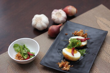 Egg with Tamarind Sauce in a white plate served on a wooden table with coriander sprinkles, is a popular local dish that Thai people eat.