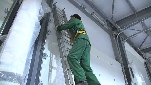 Professional worker climbing up ladder indoors to repair a transformer. Man in a workwear