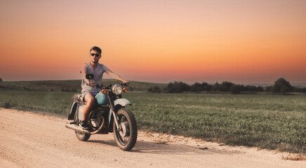 male biker rides on a retro custom motorcycle along a country road at sunset.