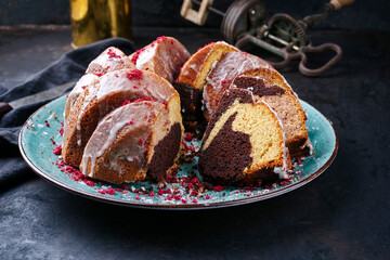 Traditional exotically bundt marble cocoa chocolate cake with icing sugar glaze and freeze dry raspberry topping served as close-up on a Nordic design plate