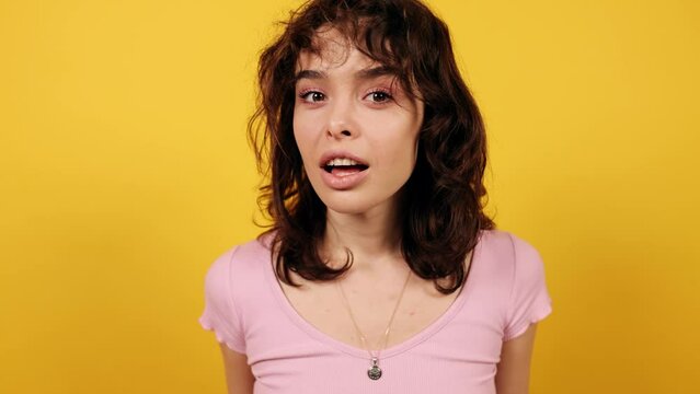 Beautiful brunette looking around and asking to be quiet with serious look. Attractive young girl on yellow background. High quality 4k footage