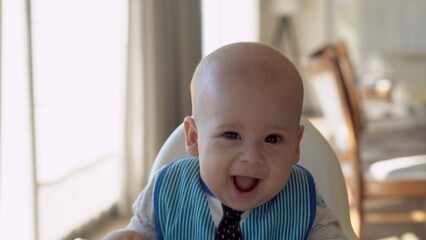 Childhood, Happiness, family, Motherhood. Cheerful happy smiling baby Close up face. Emotions of newborn boy. child in a bib sits in a feeding chair gnaws toothpick in the kitchen, Infant gum pain