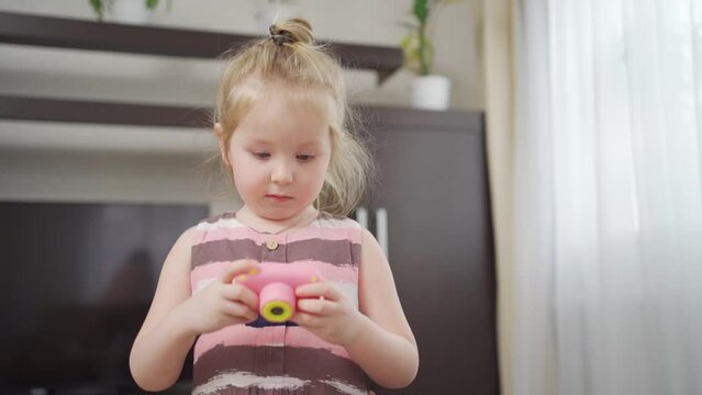 a funny little girl takes a photo on a little pink toy camera. 