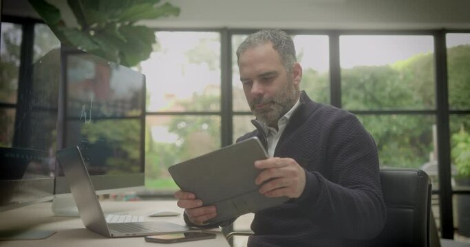 Male Stockbroker Looking at Digital Tablet Sitting at Desk at Home