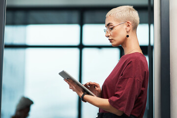 Ticking off my tasks as I get them done. Cropped shot of an attractive young businesswoman wearing spectacles and using a tablet while standing alone in her office.