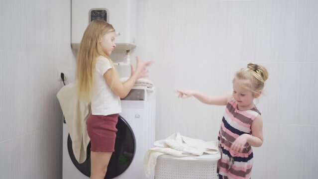 two cute and cheerful girls play with laundry in the laundry room. 
