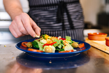 Detail of the hands of a young boss, putting ingredients on a salad plate in a professional kitchen.