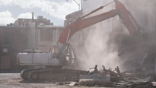 A wide view of a building demolition excavator destroying an old apartment building in a small town. Shot at 60fps for optional slow motion use. With audio.  	