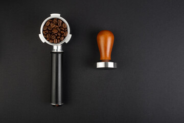 Barista Kit. Coffee Tamper with Brown Wooden Handle and coffee horn with beans. Top view on black background. Barman tool for pressing down ground coffee, a tamper for a coffee machine
