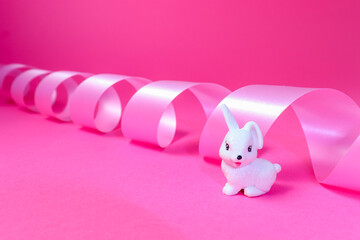Little white rabbit and pink ribbon on pink background