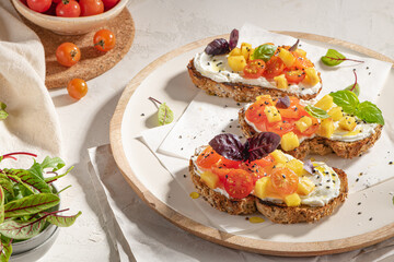 Italian bruschettas with roasted tomatoes, cream cheese, pineapple slices and herbs on a kitchen countertop. Prepared to serve