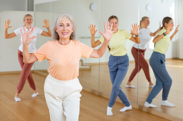 Portrait of elderly smiling european woman and people dancing in modern studio