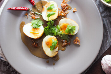 Egg with Tamarind Sauce in a white plate served on a wooden table with coriander sprinkles, is a popular local dish that Thai people eat.