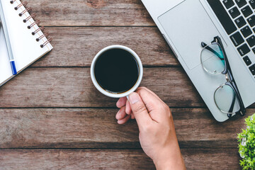Male hand hold mug of coffee on wood table.