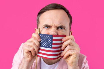 Portrait of a satisfied young man with a beard with an American flag on a red studio background. Great US patriot and defender of freedom.