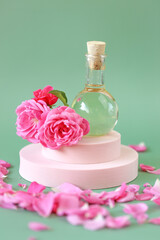 Rose essential oil in a glass bottle in rose flowers in rose petals on a pink podium on a green background. natural rose oil.Organic bio cosmetics 