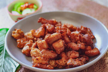 Fried Pork Belly with Fish Sauce and Sticky Rice Served on a white plate on a black wooden floor.