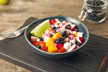 Board with bowl of Mexican vegetable salad on wooden background