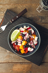 Board with bowl of Mexican vegetable salad on wooden background