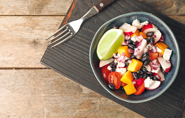 Board with bowl of tasty Mexican vegetable salad on wooden background