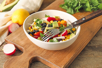 Board with bowl of tasty Mexican vegetable salad on wooden table