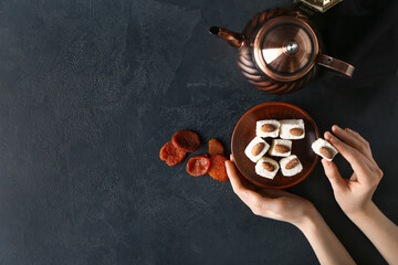 Female hands with tasty Turkish delight, dried apricots and tea on dark background