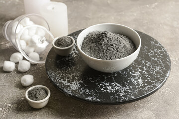 Bowls of activated carbon powder for facial mask and cotton balls on grunge background