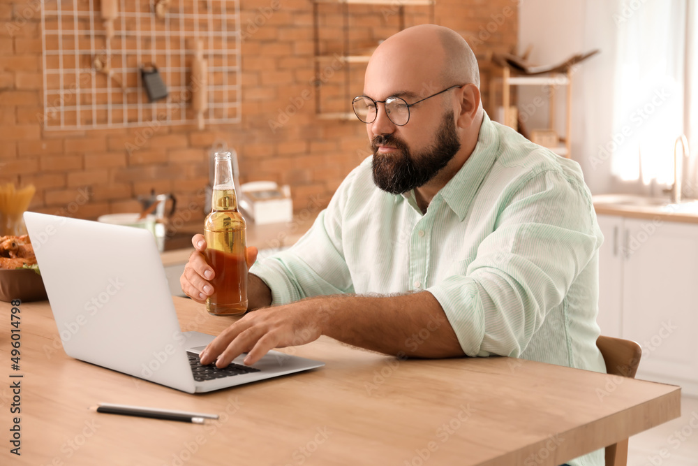 Wall mural Bald man with laptop drinking beer in kitchen