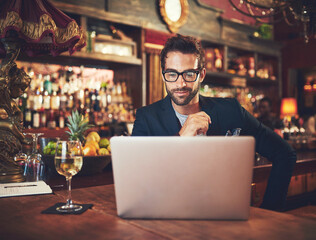 Putting the final touches on his latest article. Cropped shot of a young man using his laptop while sitting in a bar.