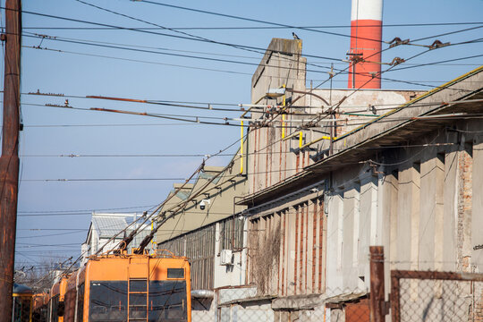 Power pole and pantograph of a trolleybus connecting vehicle to electrical cable line, the overhead cable, or catenary in a neglected industrial background in a worskhop depot. ..