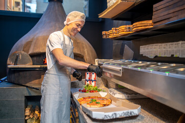 A chef in apron and hair cap preparing pizza