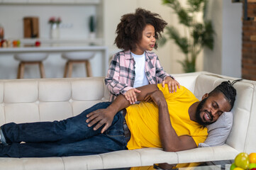 Man lying with closed eyes and touching cute daughter