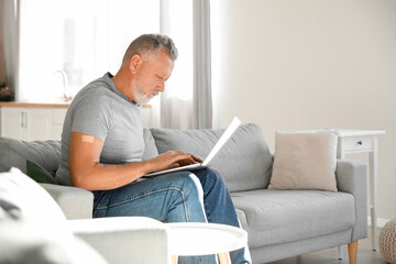 Mature man with applied nicotine patch using laptop at home. Smoking cessation