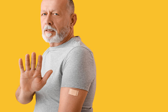 Mature man with applied nicotine patch showing stop gesture on color background. Smoking cessation