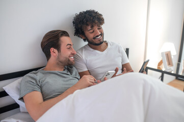 Obraz premium Gay couple using their gadgets in the bedroom