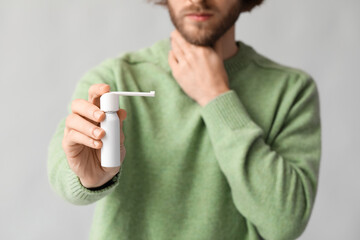Ill man with inhaler on grey background, closeup