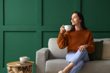 Beautiful young woman with cup of tea resting on couch at home