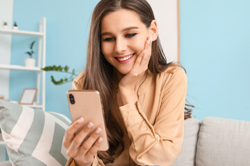 Beautiful young woman with mobile phone reading message at home
