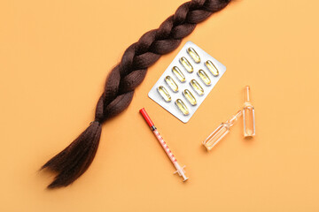 Braided hair strand with pills, syringe and ampules on orange background