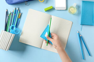 Child's hand with different stationery and bottle of sanitizer on color background