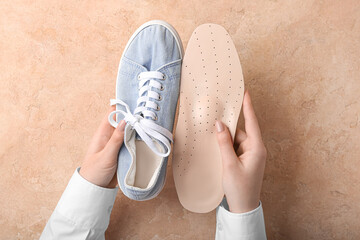 Female hands with beige orthopedic insole and shoe on beige background