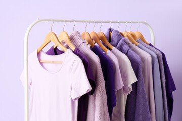 Rack with clothes in purple shades on lilac background