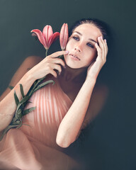 A large portrait of a woman holds a lily shot on the surface of the water. Born again. Meaning of Being