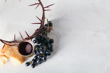Cup of wine with grapes, bread and crown of thorns on light background