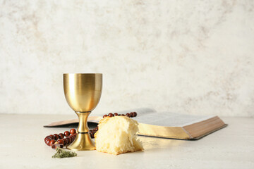 Cup of wine with bread, rosary and Holy Bible on light background
