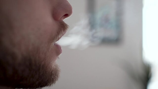 Male person smoking a cigarillo. This is his unhealthy daily habit. Footage for topics like cigarette smoke, nicotine addiction, health danger, lung cancer, bad smell, slow death, physical illness.