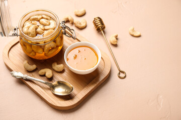 Jar of tasty cashew nuts with honey on beige background