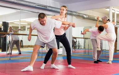Concentrated sporty young woman learning self defence techniques in sparring with man, practicing...