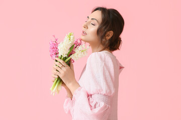 Pretty young woman with hyacinth flowers on pink background